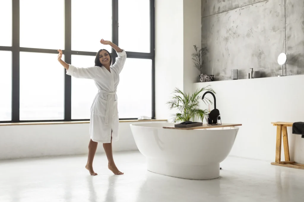 Woman enjoying a bright, modern bathroom with freestanding soaking tub and minimalist concrete wall—Truxtun custom home design in St. Simons Island, GA