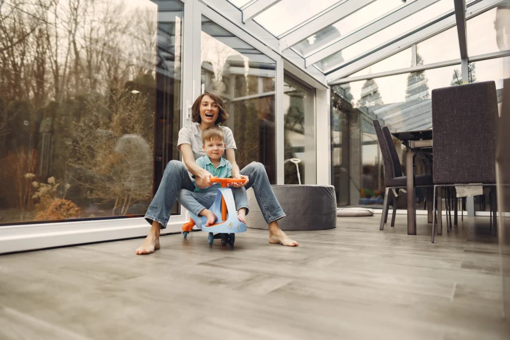 Mother and child playing in a glass-enclosed sunroom with modern flooring—Truxtun home addition in St. Simons Island, GA