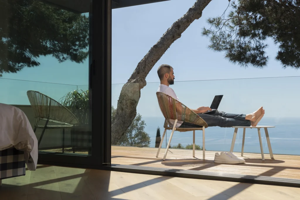 Man working on a laptop from a balcony with coastal ocean view—Truxtun home built for indoor-outdoor living in St. Simons Island, GA