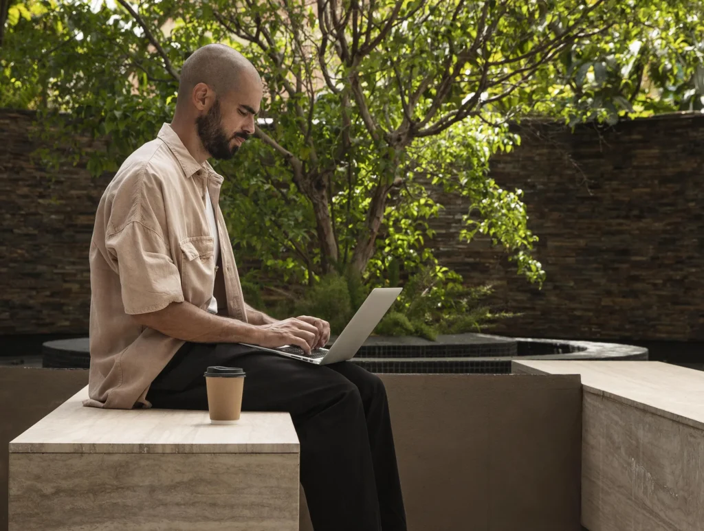 Bearded man working on a laptop in a modern outdoor seating area—Truxtun-designed landscape with remote work comfort