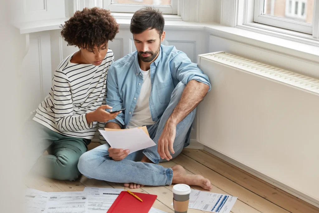Young couple reviewing home plans while seated on hardwood floors—Truxtun new home construction consultation