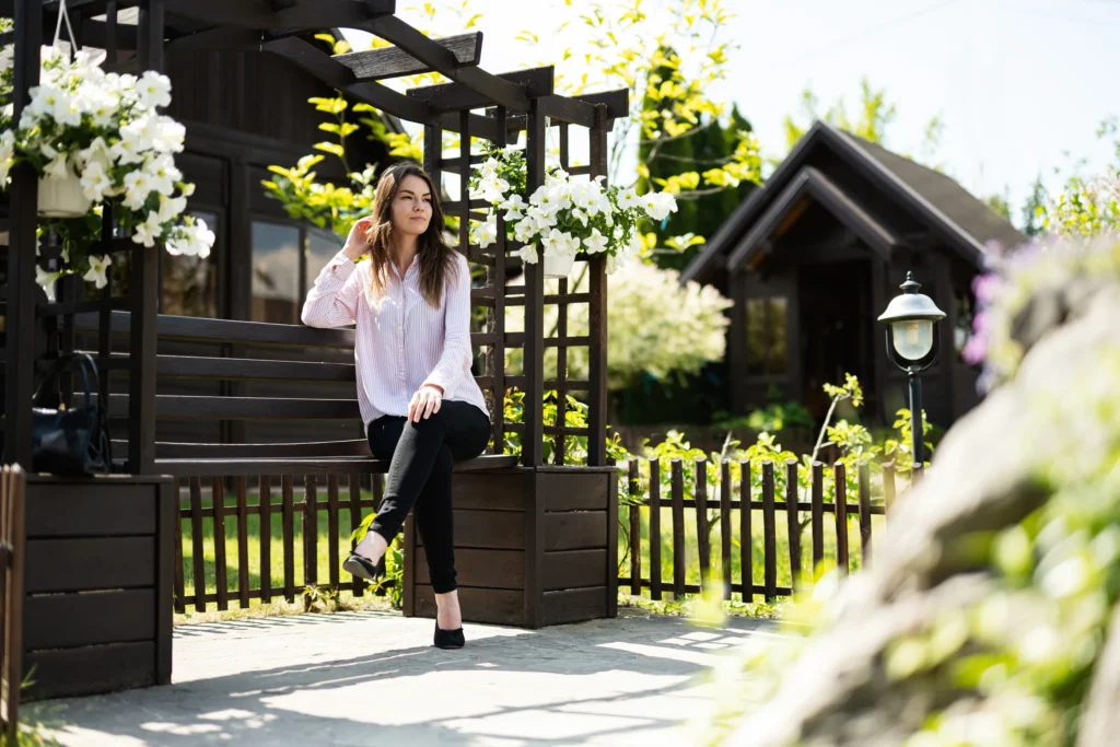 Woman relaxing on a sunny backyard patio with wooden pergola and garden fencing—Truxtun custom outdoor living design